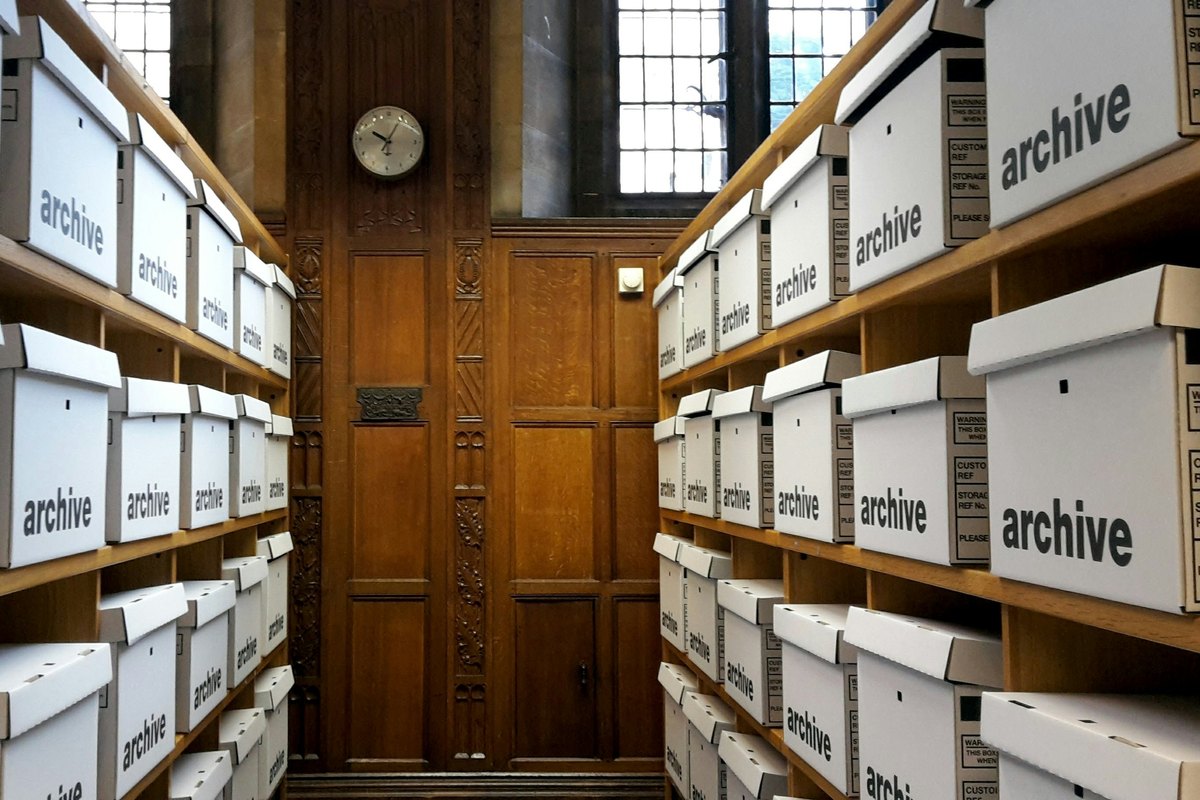 Wooden shelves stacked with white archive boxes on both sides of a narrow room