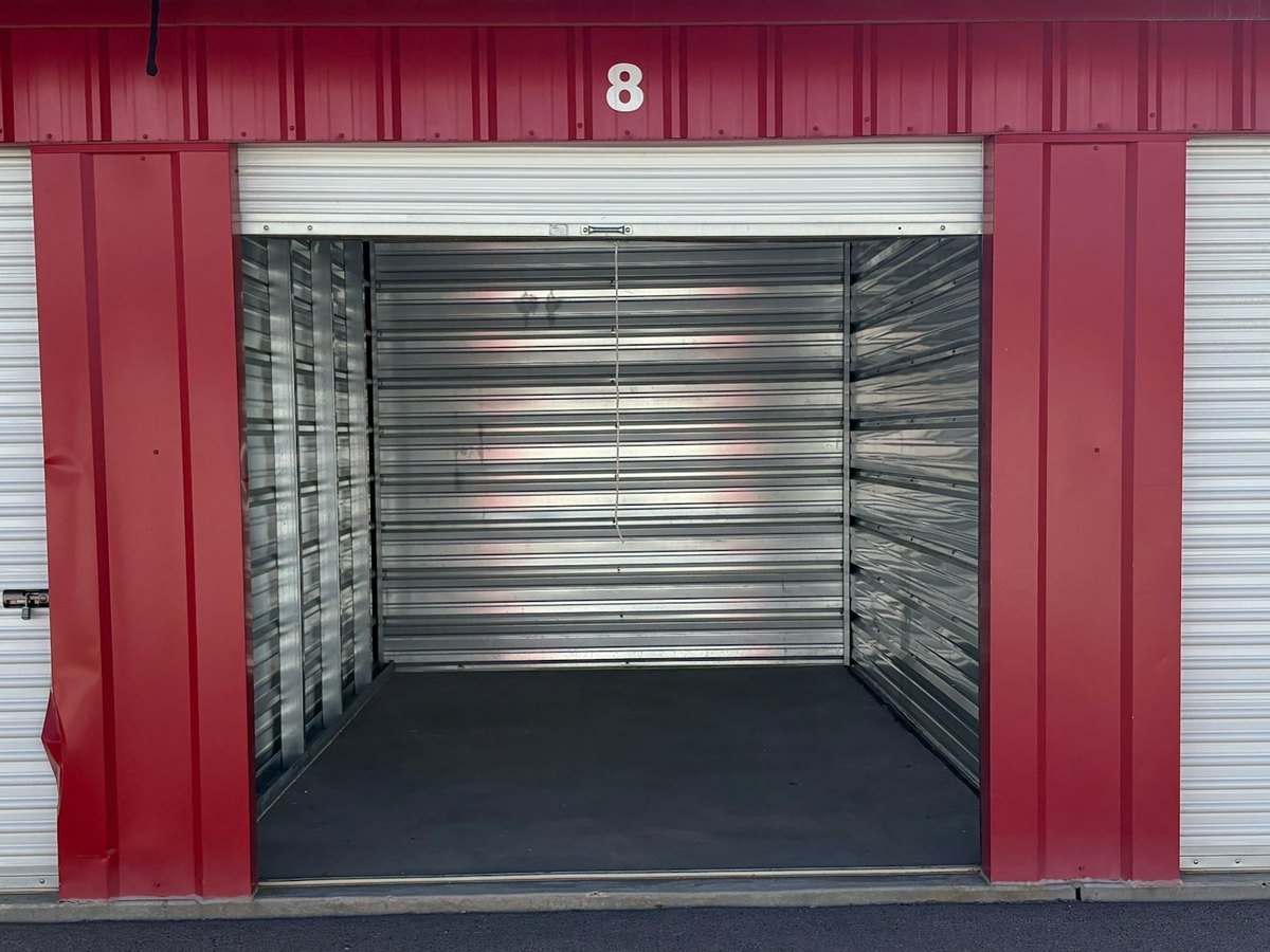 Close view of an open, empty storage unit numbered 8 with silver metal walls and red trim